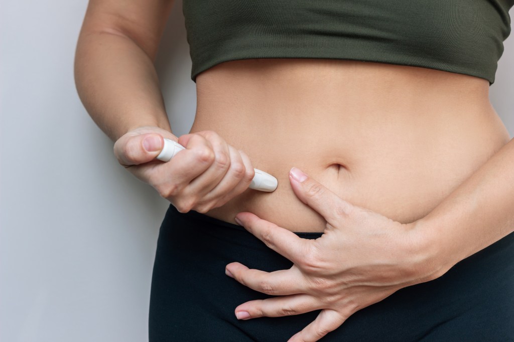 A woman injecting her stomach with a pen syringe.