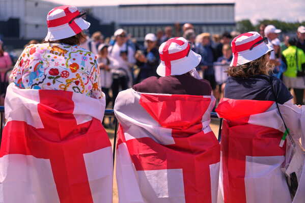 Spectators wrapped with England flags watch the third round of the Women's British Open golf championship in Lytham St Annes, England, Saturday, Aug. 1, 2026. (AP Photo/Jon Super)