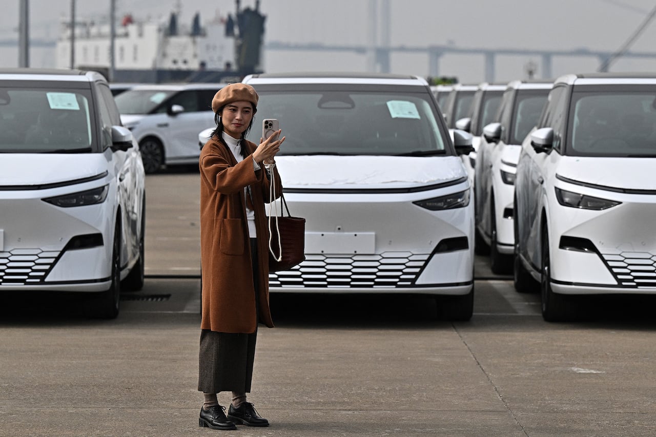 A woman takes a selfie in front of a line of cars.