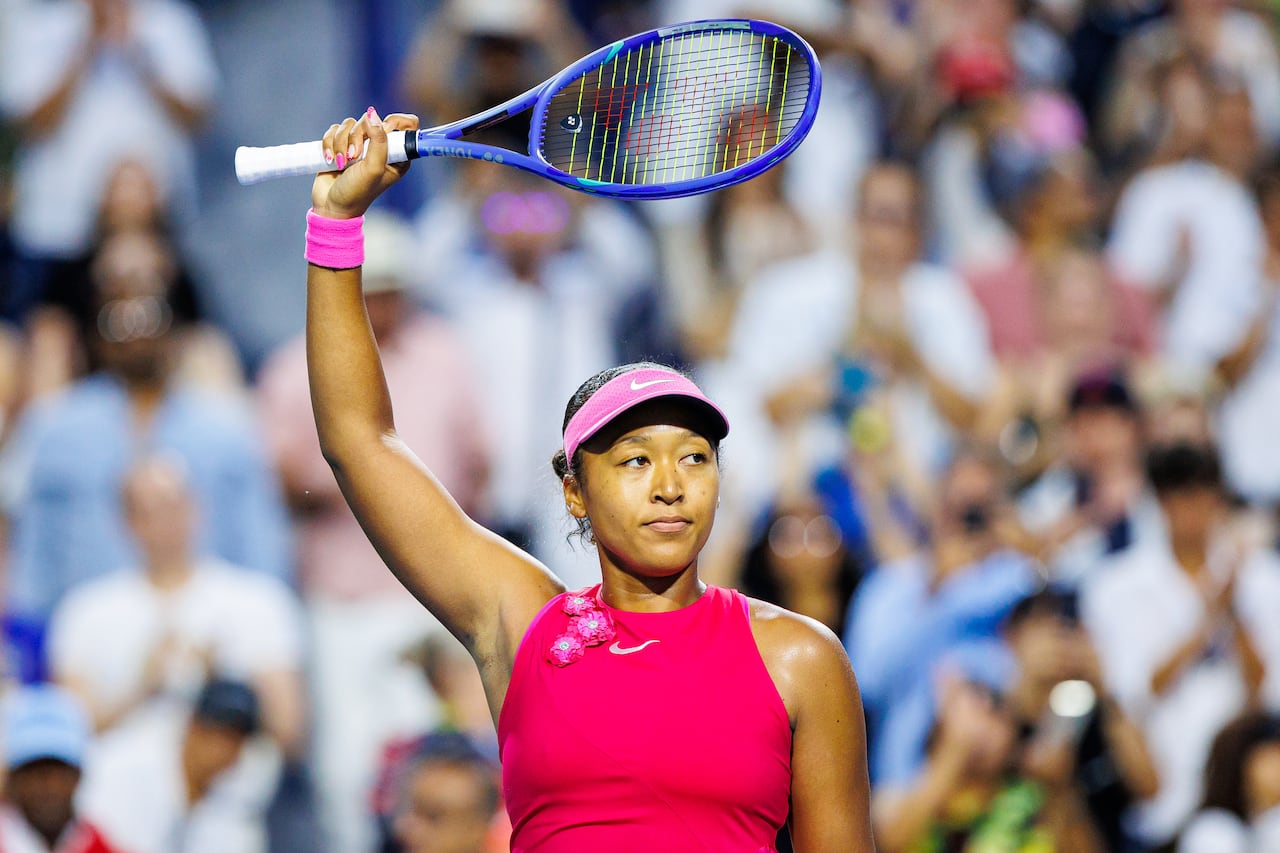 A female tennis player raises her raquet in victory at the end of a match.