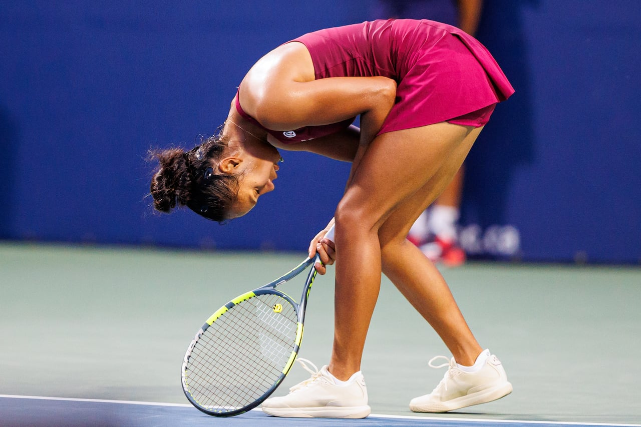 A female tennis player doubles over with her raquet on the ground during a tennis match.