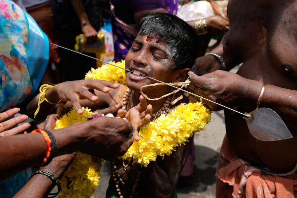 A Hindu devotee reacts in pain after having his cheeks pierced with a steel rod as part of a ritual during the 'Aadi' festival, a holy month for Tamils observed with prayers and offerings to Hindu goddesses, in Chennai, India, Sunday, Aug. 9, 2026. (AP Photo/Mahesh Kumar A.)