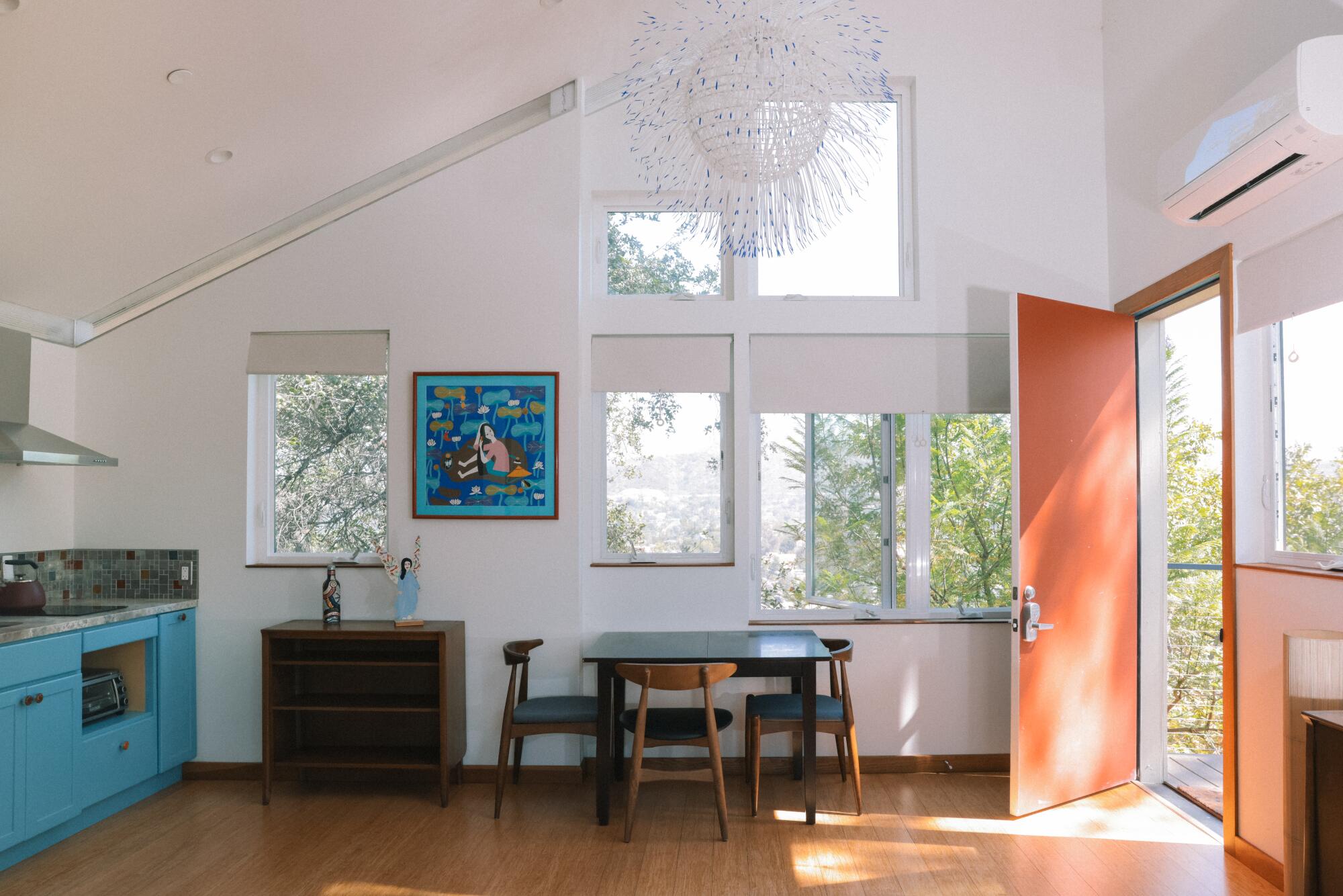 The interior of an ADU with an orange door, blue kitchen cabinets and colorful art.