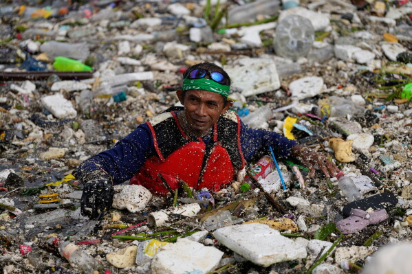 A worker tries to clear a sea of garbage and debris brought by intense monsoon rains at the Redemptorist Water Channel in Paranaque city, Metro Manila, Philippines Tuesday, Aug. 11, 2026. (AP Photo/Aaron Favila)