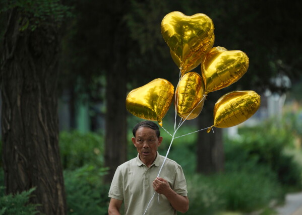 A man holds balloons as he walks on a sidewalk in Beijing, Tuesday, Aug. 11, 2026. (AP Photo/Achmad Ibrahim)