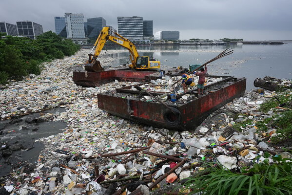 Workers carry bamboo beside a sea of garbage that was washed ashore due to intense monsoon rains, Wednesday, Aug. 12, 2026, in Pasay city, Metro Manila, Philippines. (AP Photo/Aaron Favila)