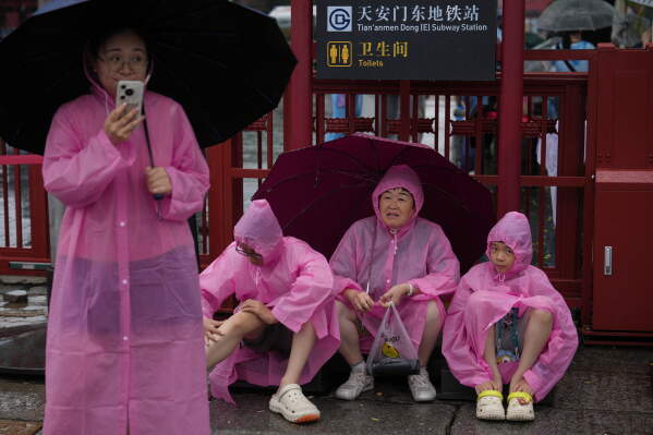 People wearing rain covers rest as they visit the Forbidden City during a rainy day in Beijing Wednesday, Aug. 12, 2026. (AP Photo/Andy Wong)