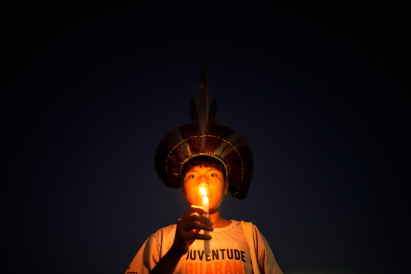 An Indigenous youth holds a candle during a protest calling for the protection of Indigenous land rights and demarcations outside the Supreme Court in Brasilia, Brazil, Tuesday, Aug. 11, 2026. (AP Photo/Eraldo Peres)