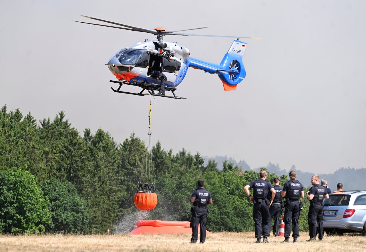 Police officers observe a helicopter loading water.