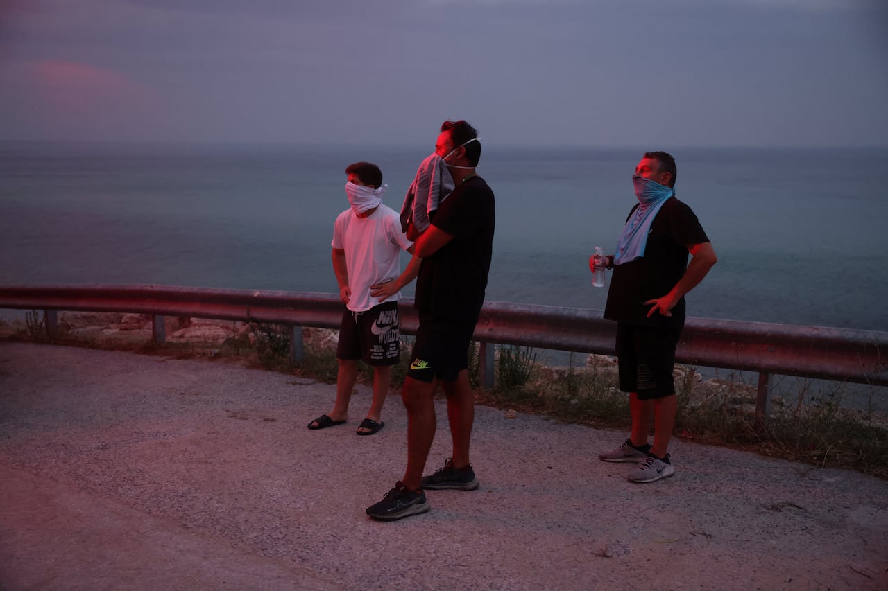 Three men with cloths covering their faces stand on a road.