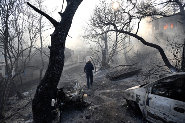 A firefighter walks through a burned area as flames engulf a house during a wildfire on the island of Salamina, west of Athens, Greece, Sunday, Aug. 16, 2026. (AP Photo/Michael Varaklas)