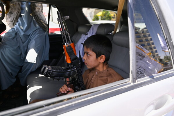 A boy holds an AK-style rifle while sitting in a vehicle decorated with Taliban flags during celebrations marking the fifth anniversary of the U.S. withdrawal from Afghanistan and the Taliban's return to power, in Kabul, Afghanistan, Saturday, Aug. 15, 2026. (AP Photo/Nava Jamshidi)