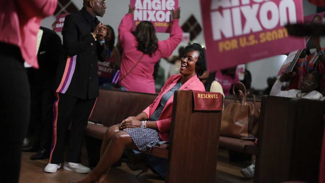 Florida state Rep. Angie Nixon sits in a church pew during a worship service as people around her hold up signs that read "Angie Nixon for U.S. Senate."