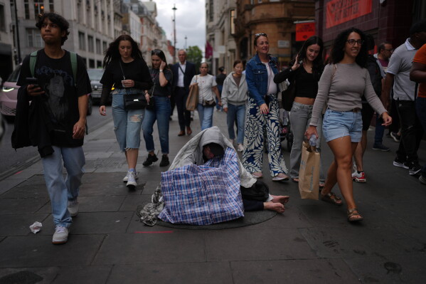 A homeless man sits on a street in a shopping district in central London, Wednesday, Aug. 19, 2026. (AP Photo/Kin Cheung)