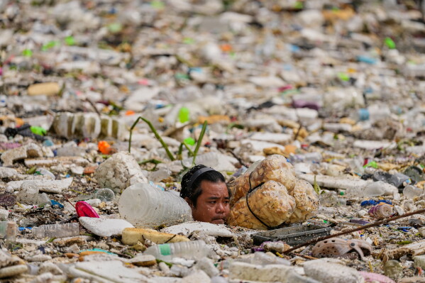 A worker uses improvised floats while trying to clear a sea of garbage and debris brought by intense monsoon rains at the Redemptorist Water Channel in Paranaque city, Metro Manila, Philippines, Aug. 11, 2026. (AP Photo/Aaron Favila, File)