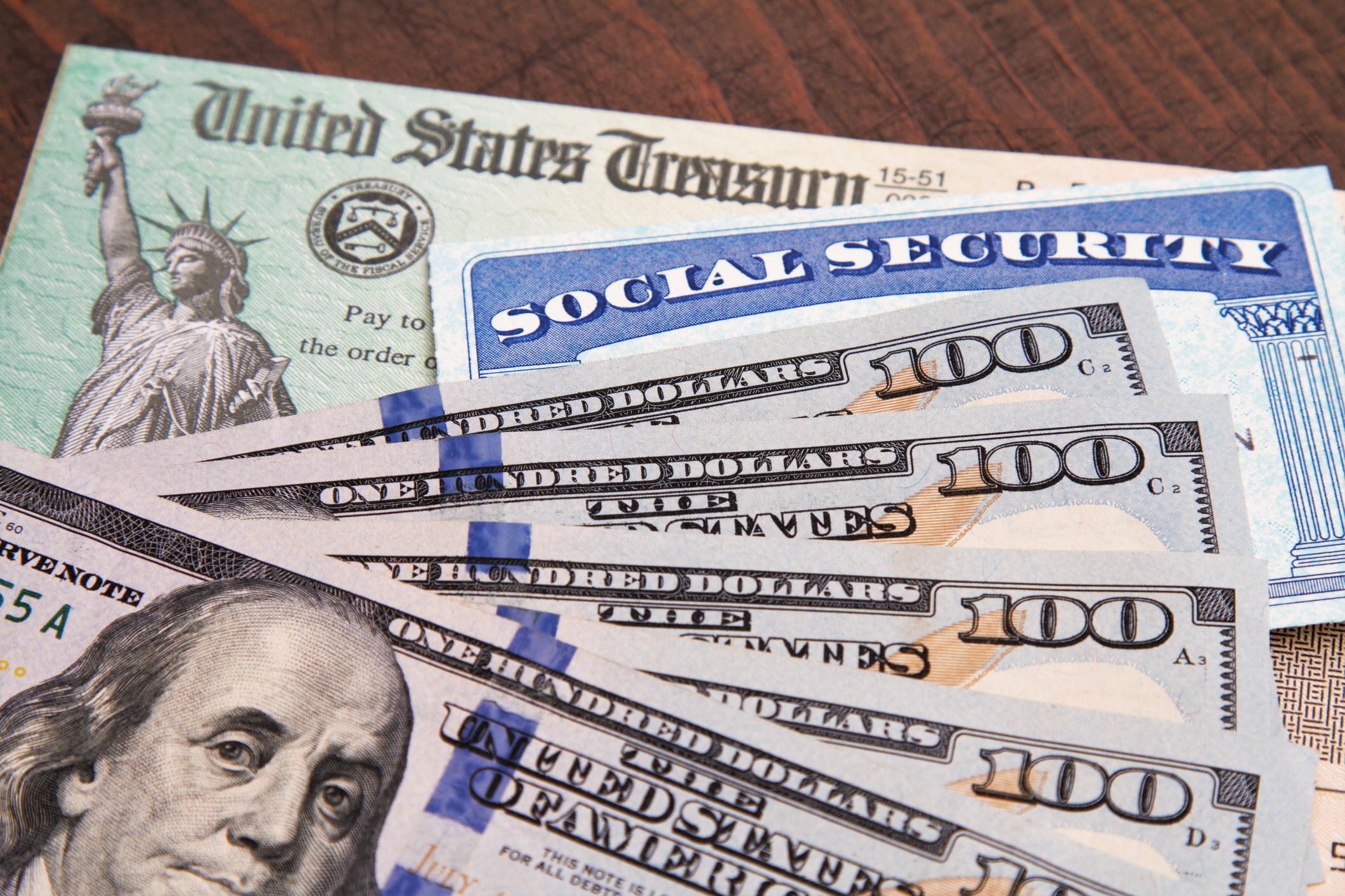 A U.S. Treasury check, a Social Security card, and U.S. currency spread over a wood surface.