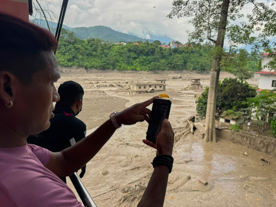 People take photographs and videos of the swollen, debris-choked banks of the Trishuli River after a flash floods in Nepal's Nuwakot district on Wednesday, Aug. 26, 2026.