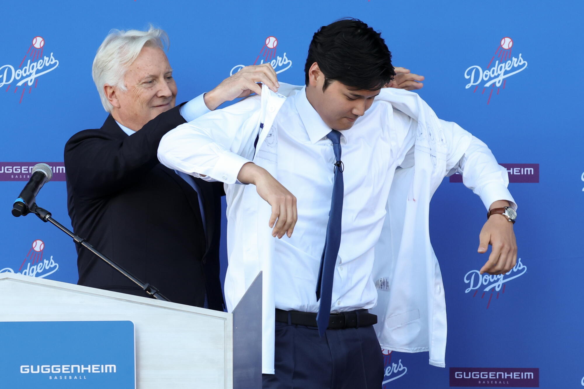 Dodgers owner Mark Walter helps Shohei Ohtani put on a jersey during a news conference.