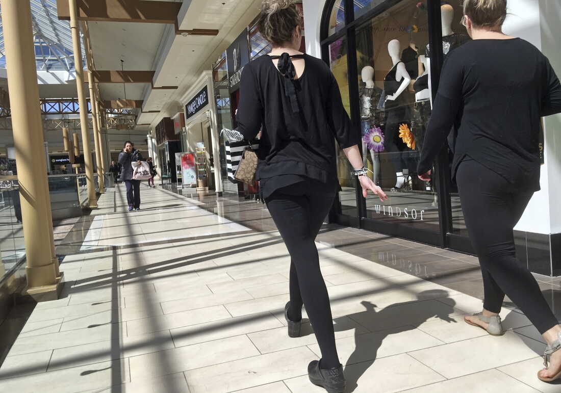 People walk inside a mall, past a row of stores.