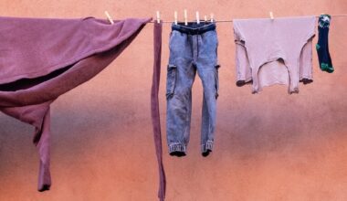 Purple fabric, jeans, a pale shirt, and a single sock hang from a clothesline against a salmon-pink stucco wall. ©CynthiaGladis