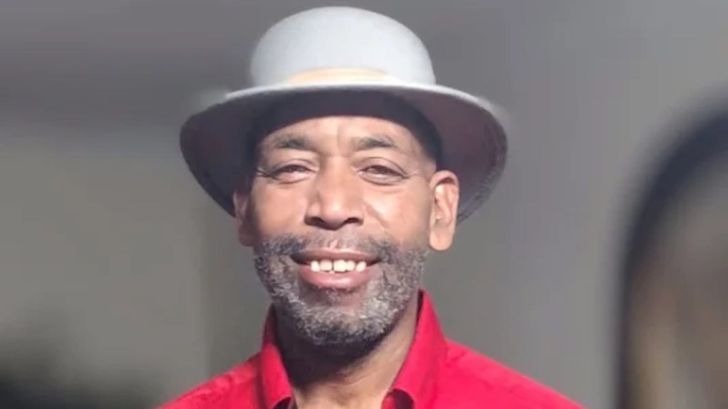 Norris Brown, an African American man with a gray beard and a gray fedora, smiles at the camera.