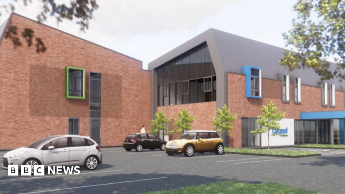 The building is low level and has brown  brick coloured walls, with two wings in the image. There is a car park with cars in the foreground.