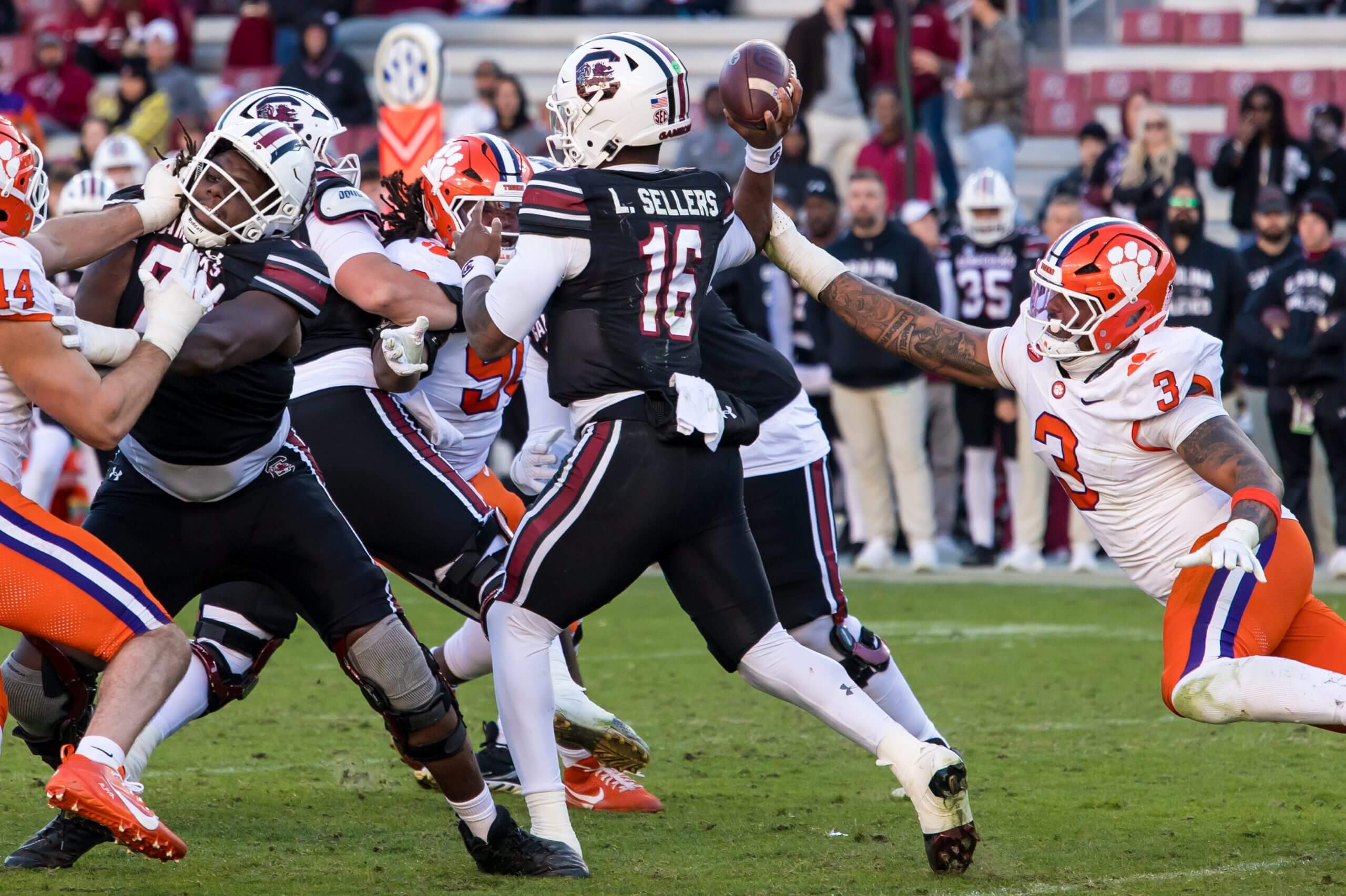 LaNorris Sellers passes the ball with a defender grabbing his arm.