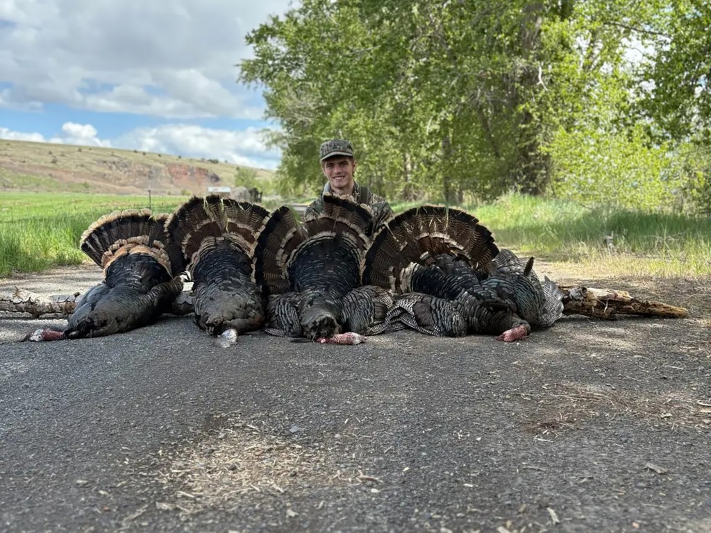 Carter J. Hickey poses with five dead wild turkeys lined up on the ground.