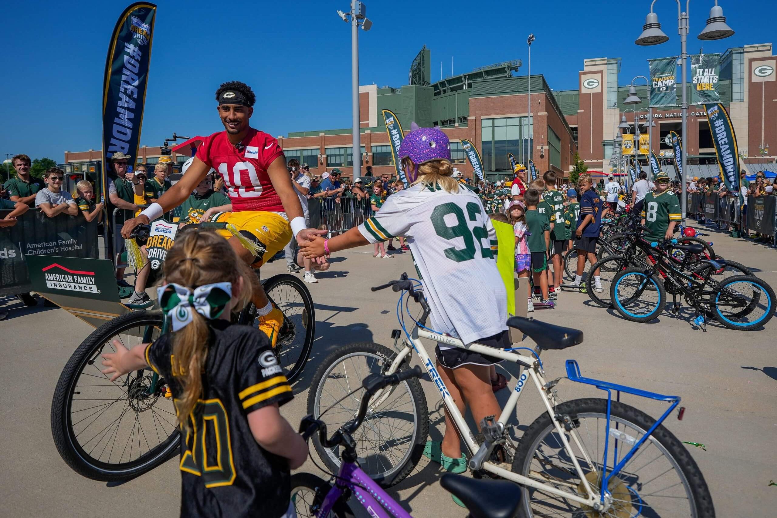 Green Bay Packers quarterback Jordan Love (10) slaps hands with young fans as he rides a bicycle to practice during the first day of training camp on Wednesday, July 29, 2026, at Lambeau Field in Green Bay, Wis.