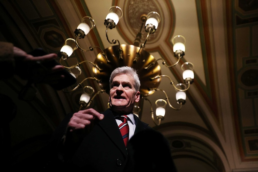 A man in a suit speaking below a chandelier