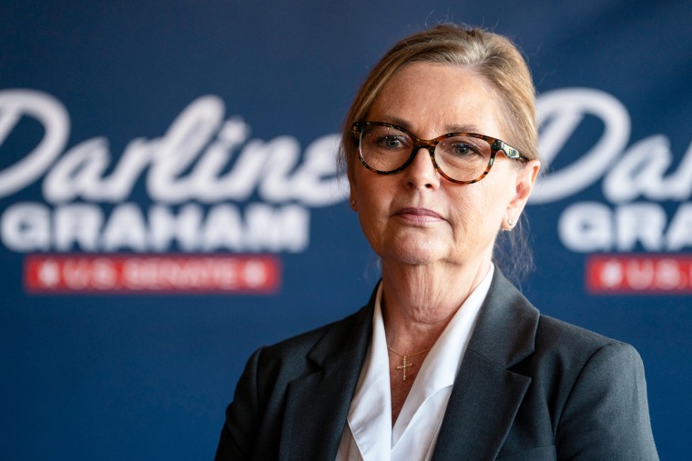 Darline Graham stands in front of a blue backdrop that reads "Darline Graham - U.S. Senate" in white text