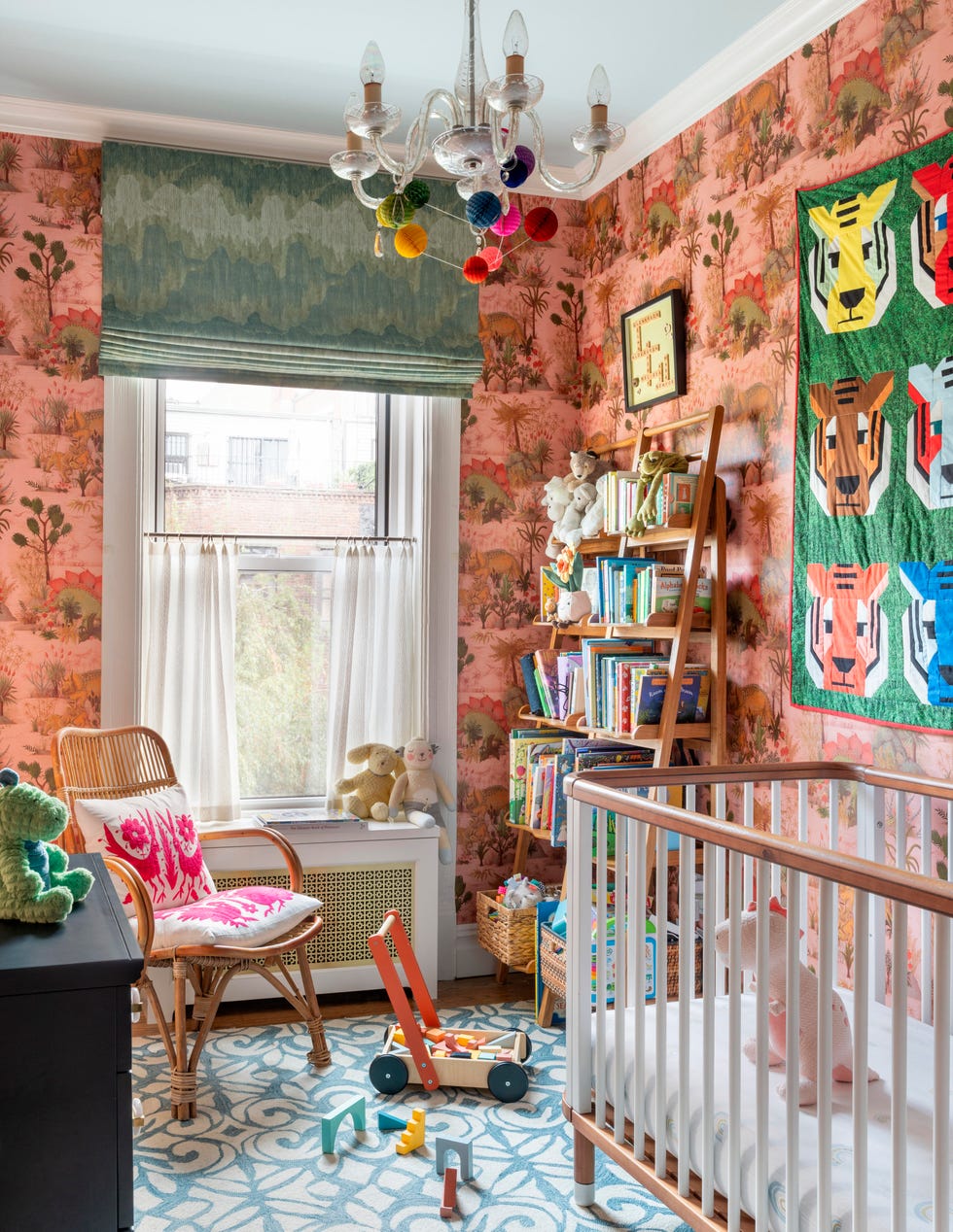 Colorful nursery with floral wallpaper, crib, bookshelf, toys, and a chandelier adorned with colorful pom-poms.