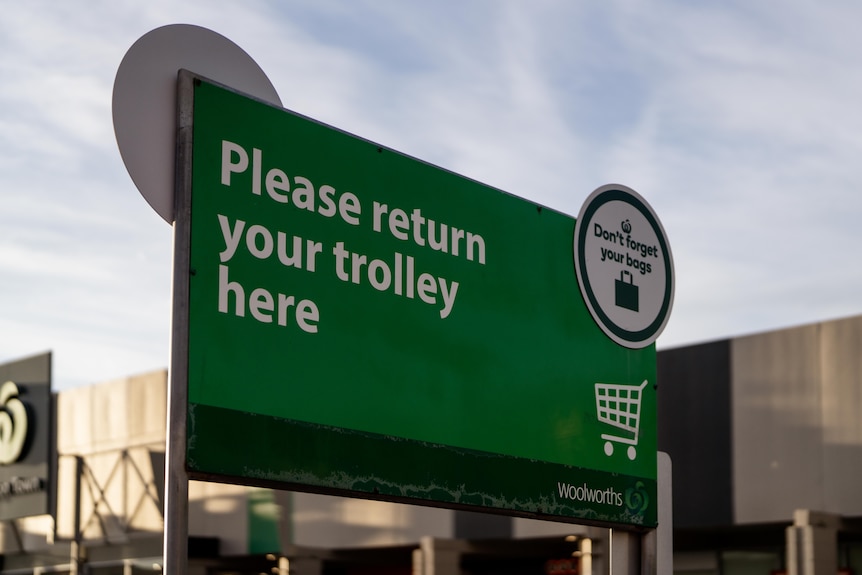 A large green sign in a grocery store carpark that says "please return your trolley here".