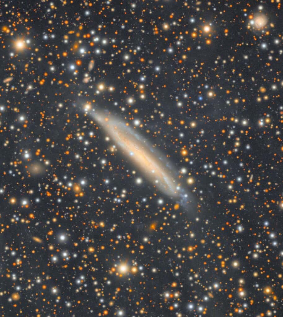 Space photo with a yellow and blue-white spiral galaxy highlighted in the middle of a cluster of stars. Vera Rubin Observatory Photo.
