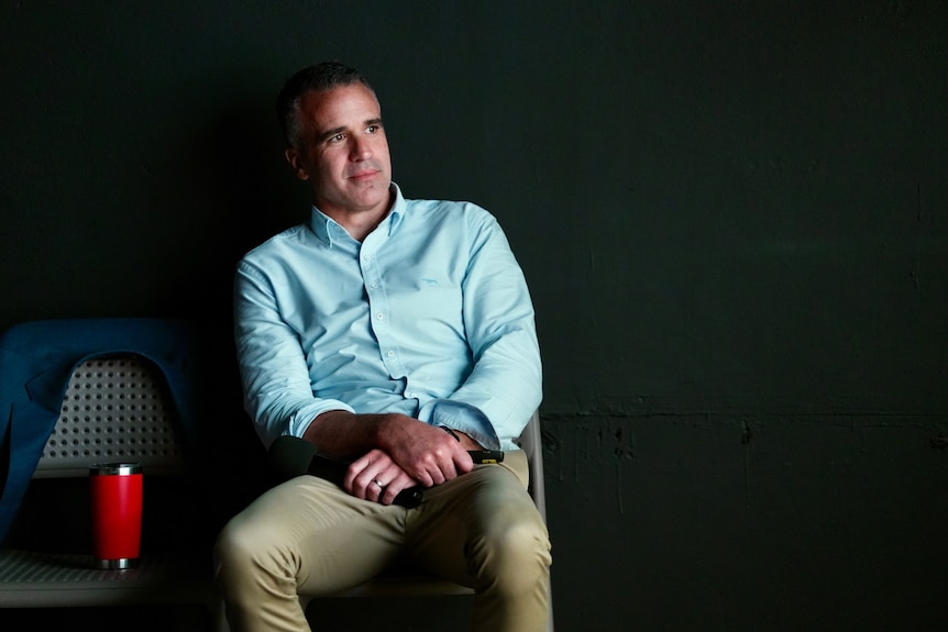 Premier Peter Malinauskas in a blue shirt sits back against a chair