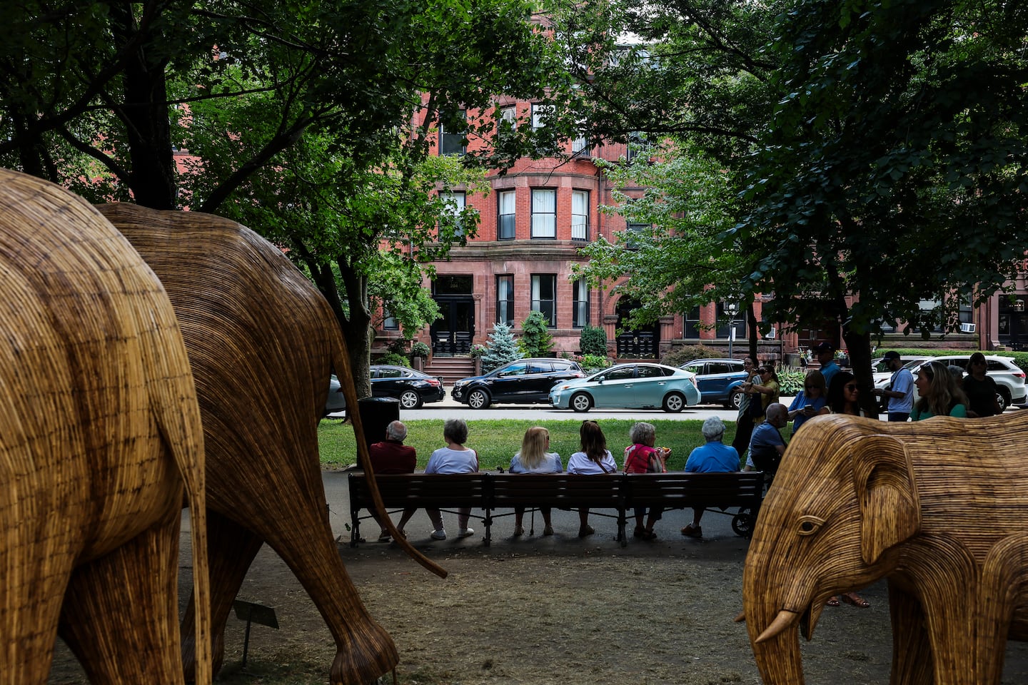 Visitors sit on a bench framed by elephant sculptures from The Great Elephant Migration and the historic brownstones lining Commonwealth Avenue in Boston’s Back Bay neighborhood on Saturday.