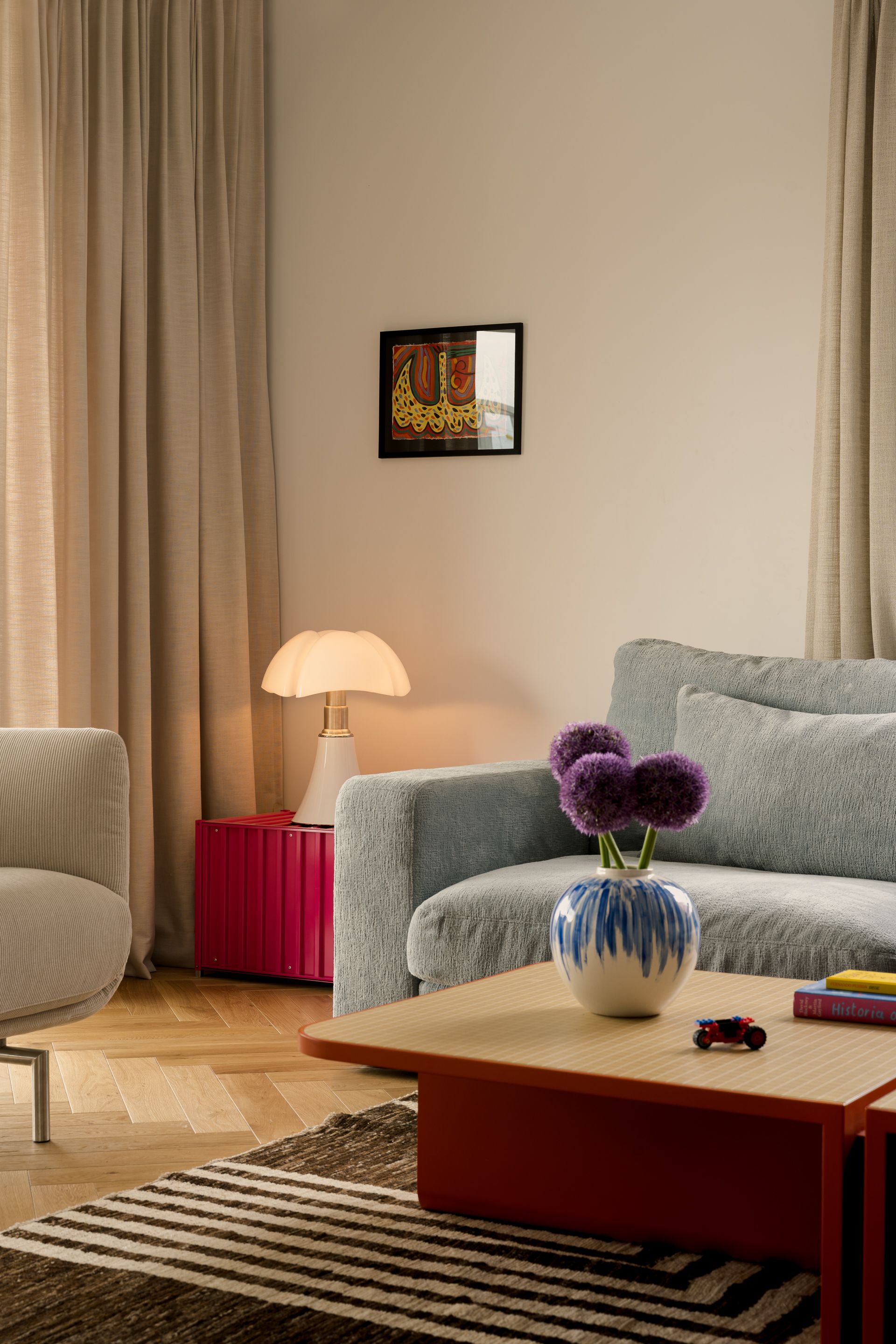 A living room plays with calm and colour at once – red tables and neutral walls