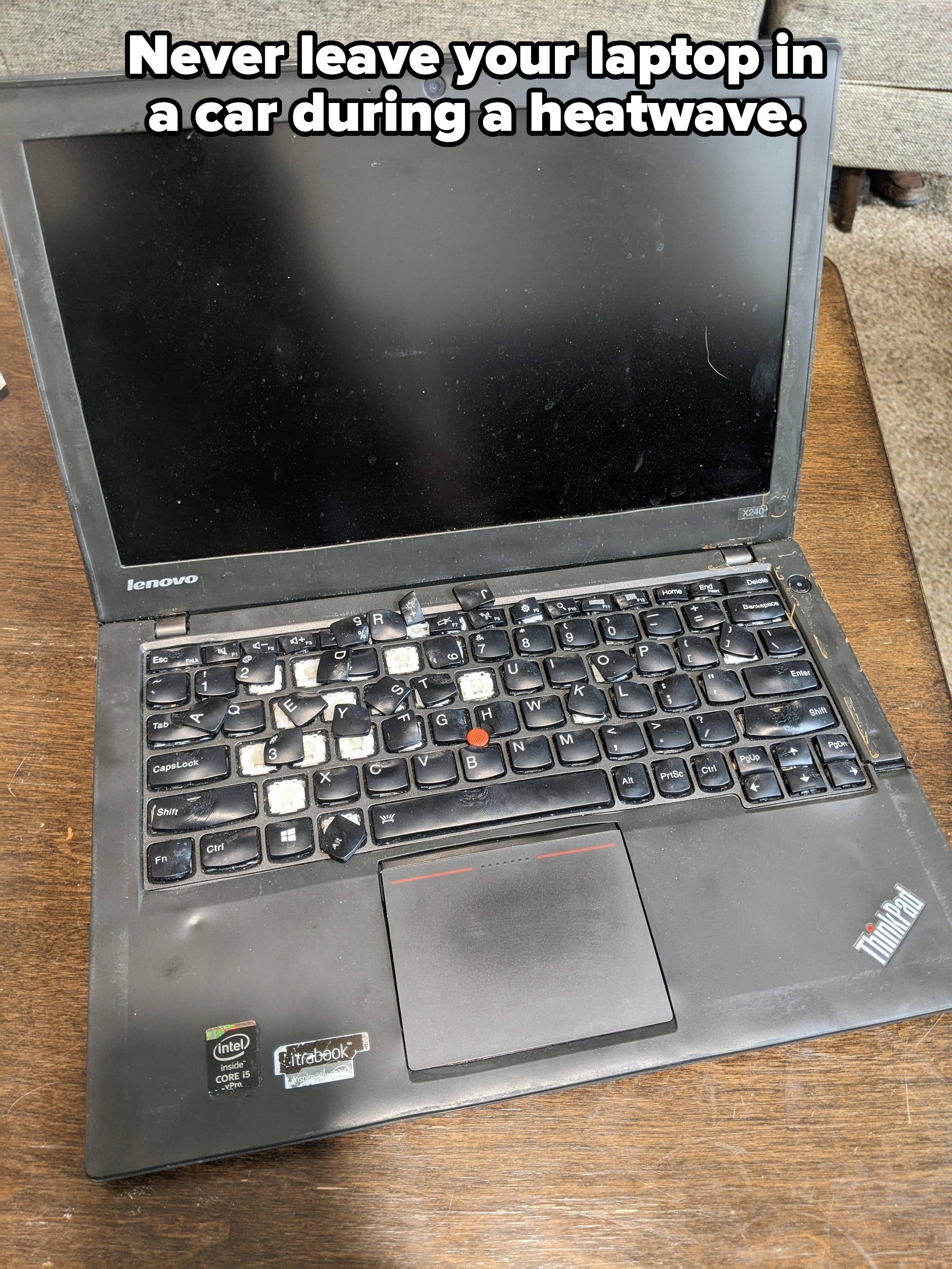 A well-used Lenovo laptop with a missing āJā key sits on a wooden table. The screen is off, and the keyboard shows signs of heavy use