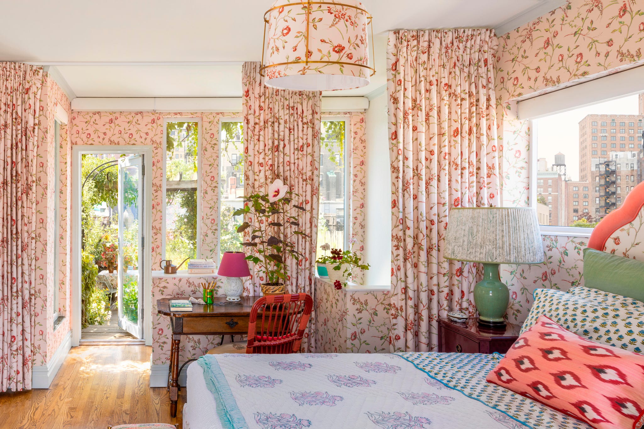 Bright and airy bedroom with floral wallpaper, a desk, and an open door leading to a garden.