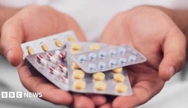 A hand holding a series of pharmaceutical drugs in packets.