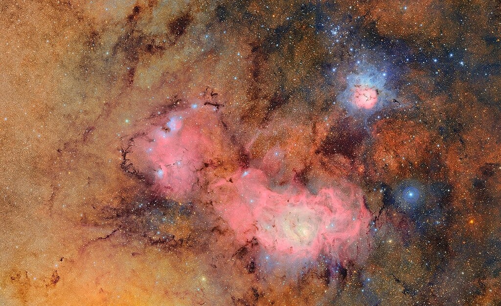 Image of the Lagoon Nebula, a pink cloud surrounded by a large brown cloud and many stars. Vera Rubin Observatory Photo.