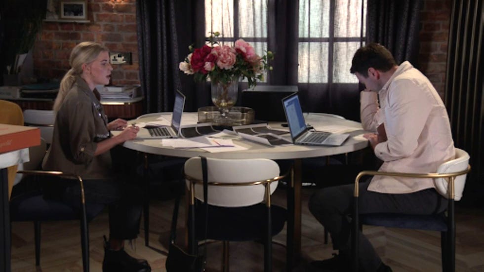 coronation street bethany kit two people working at a table with laptops and documents in a cozy room.