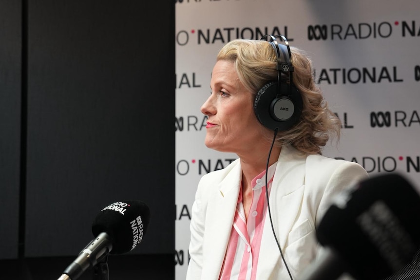 A woman wearing headphones looks forward toward a radio microphone.