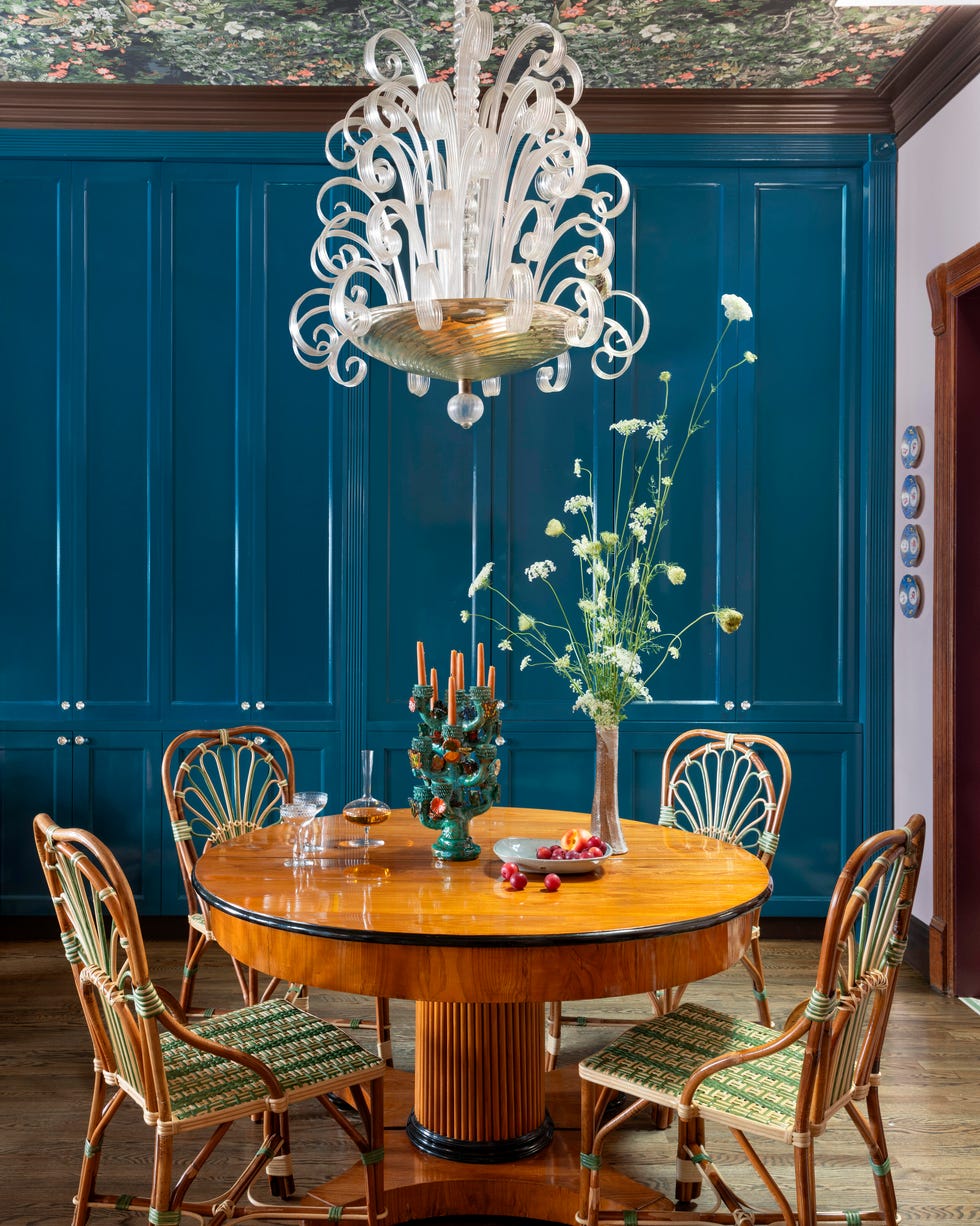 Elegant dining room featuring a round wooden table, vintage chairs, and a decorative chandelier with floral arrangements.