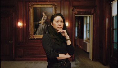 Person standing in a room with wood-paneled walls, posing thoughtfully in front of a framed portrait on the wall.