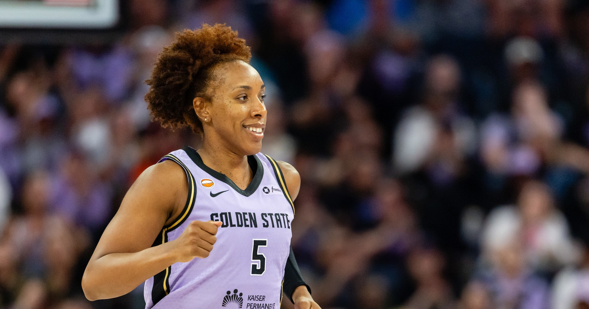 A female basketball player with curly hair, wearing a purple Golden State jersey with number 5, is running and smiling during a game.