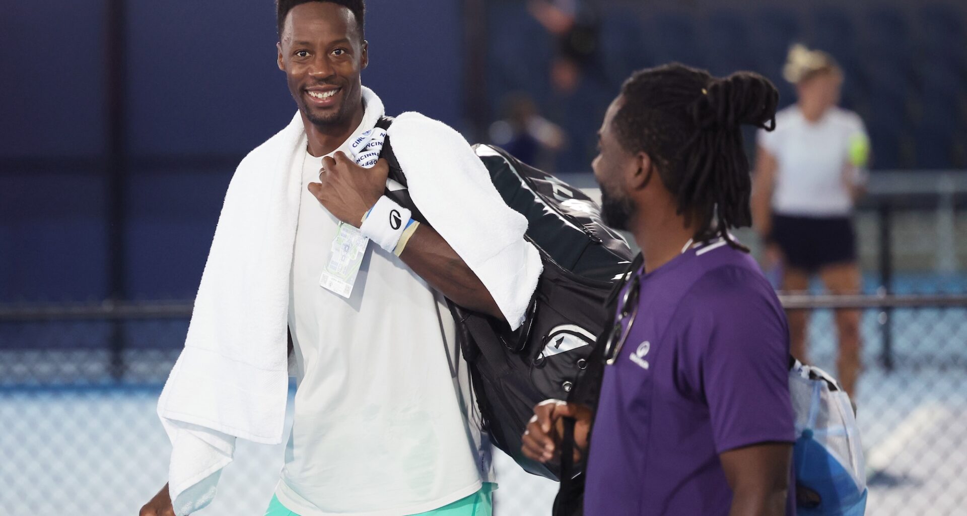 Monfils walking across the court and smiling at the camera with a towel around his neck