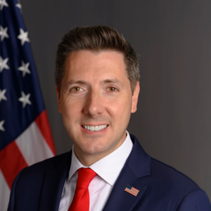 Ambassador Owens in front of the U.S. flag and a grey background