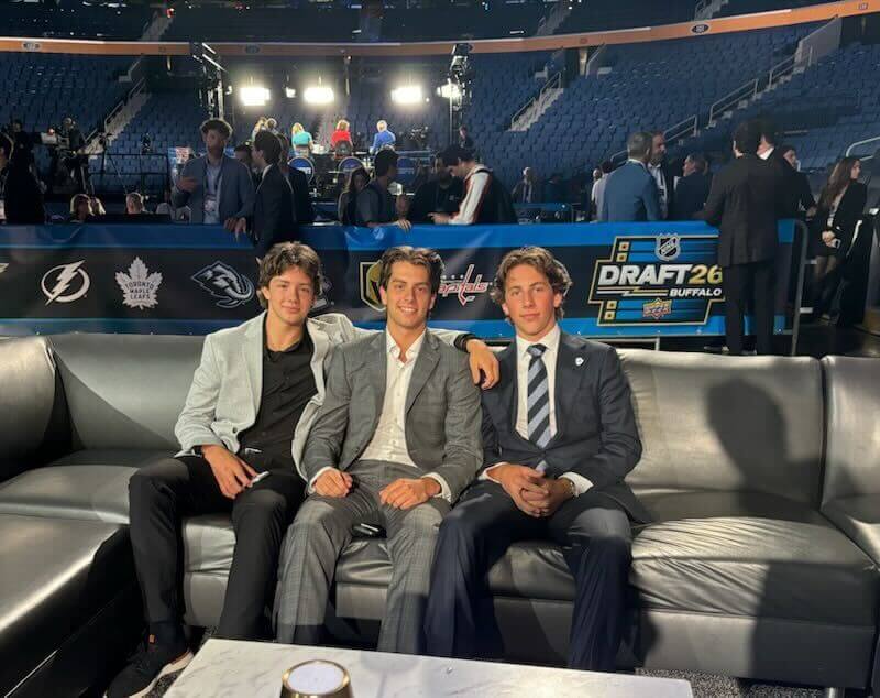 The three Cullen boys sit on a couch with part of an arena and 2026 NHL Draft in Buffalo signage in the background.