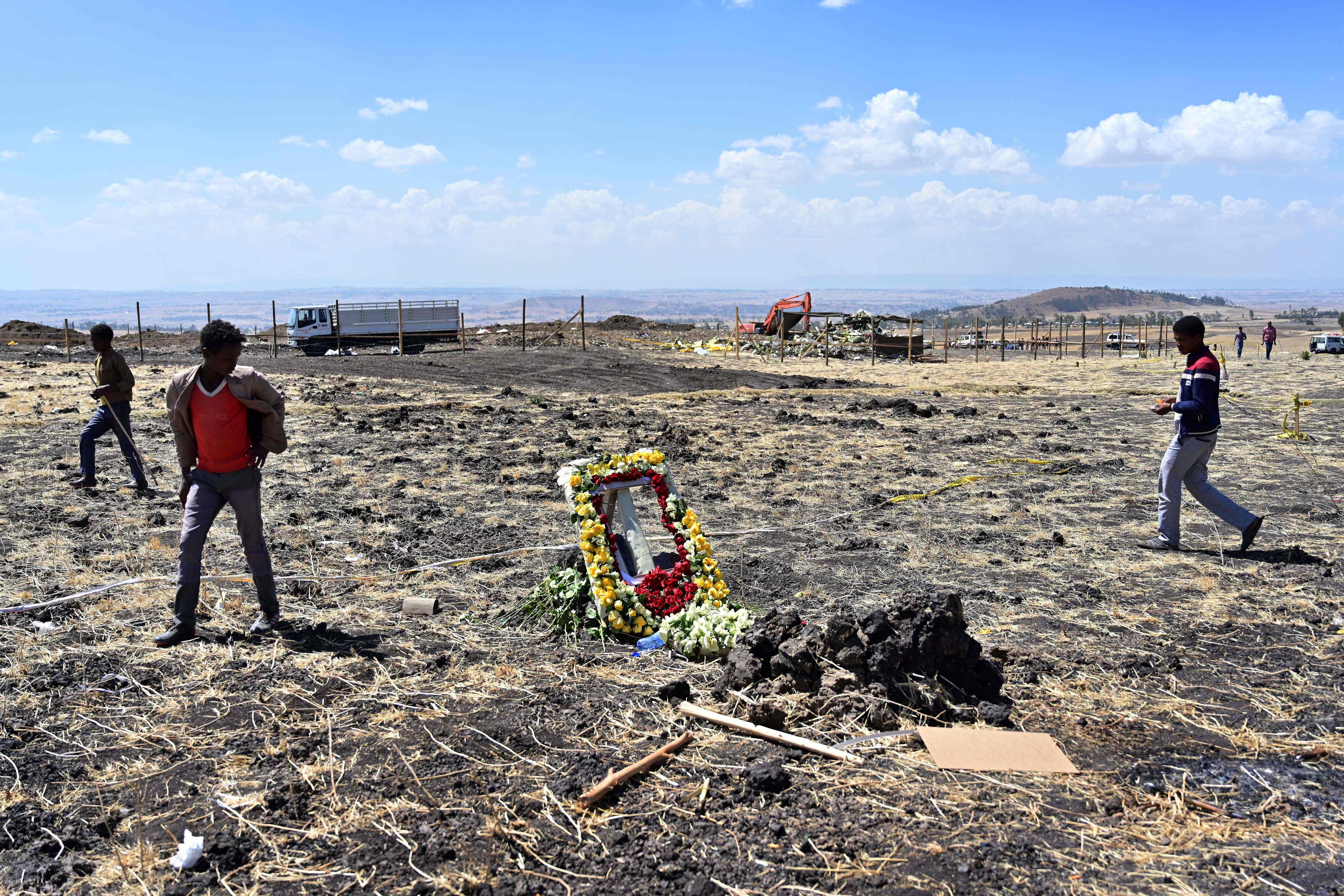People walk by a commemorative wreath left by relatives of victims at the crash site of an Ethiopian Airways-operated Boeing 737 MAX aircraft on March 16, 2019 at Hama Quntushele village near Bishoftu in Oromia region.